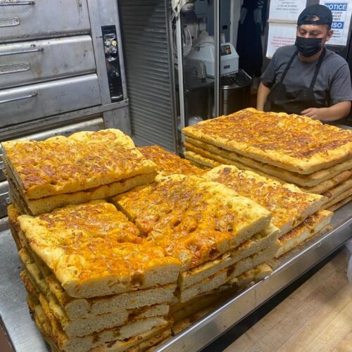 FOCACCIA stacked on prep table, just out of the oven with baker cutting it