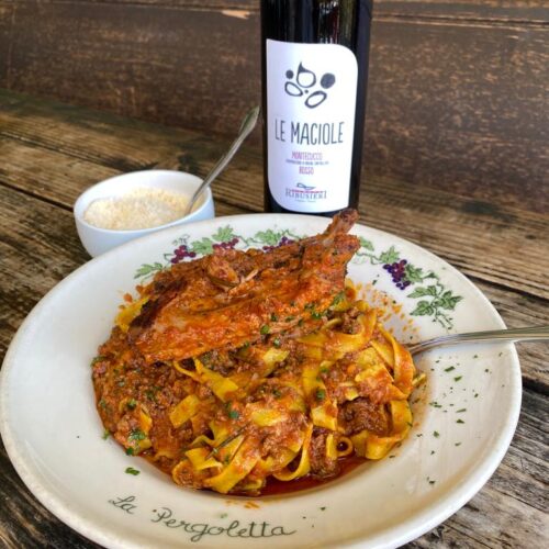 Plate of fettuccine with ragú Bolognese and pork rib ‘Ragú Bastardo’, bottle of red wine and bowl of Parmesan cheese.